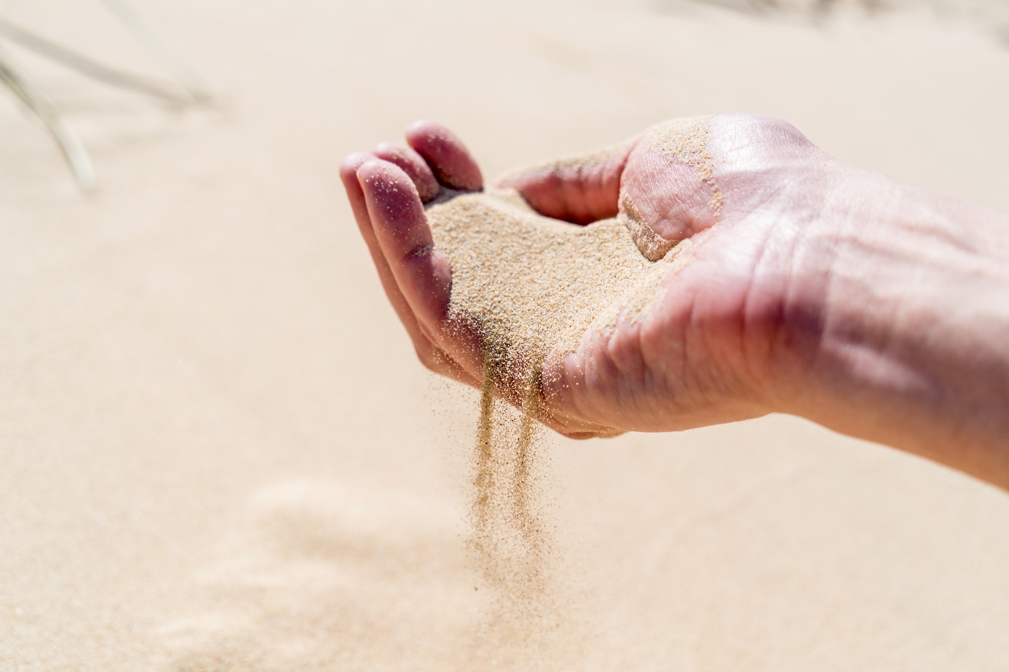 A hand pouring sand on a desert sand dune. Sand slips sifting through fingers