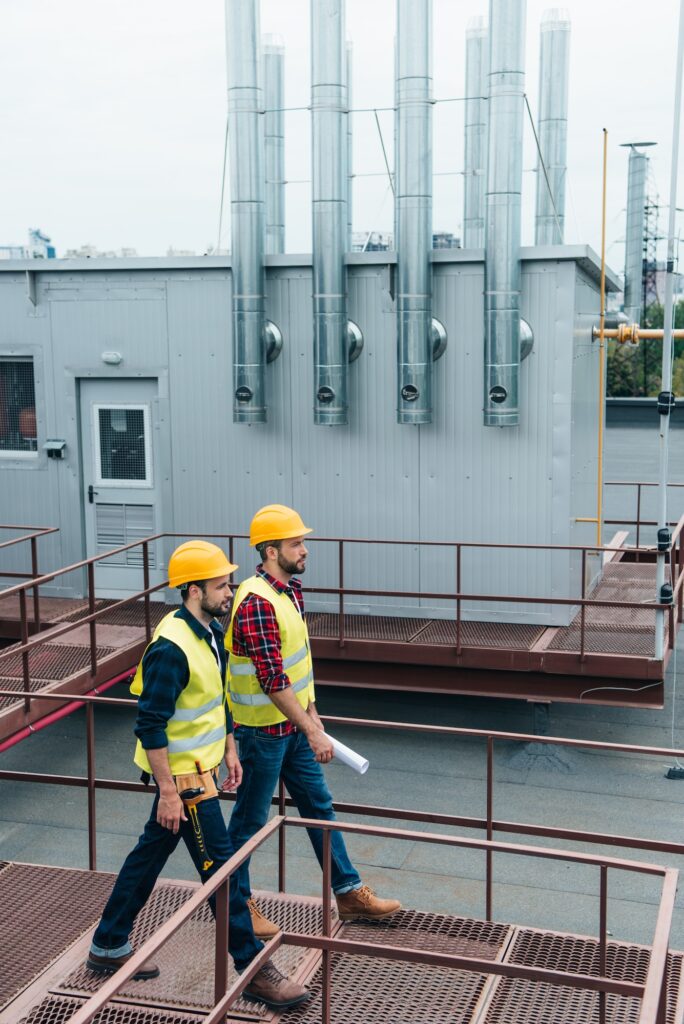 construct coworkers in safety vests and helmets with blueprint and tool belt on roof